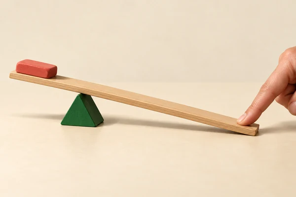 Eine Hand drückt das lange Ende eines Holzhebels; ein kleiner roter Radiergummi liegt auf dem kurzen Ende